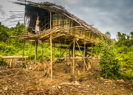 Dekai, Papua, Indonesia - September 2015: Old native man stands in his wooden house surrounded by greenery in Dekai, Papua, Indonesia. Documentary editorial.のeditorial素材