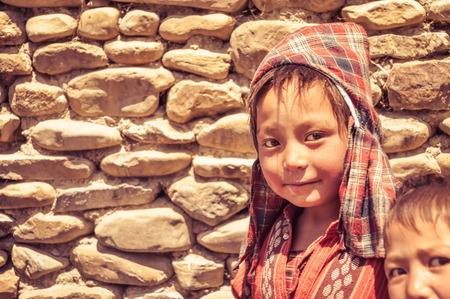 Dolpo, Nepal - circa June 2012: Small brown-haired boy with checked red headcloth and red shirt with nice brown eyes in Dolpo, Nepal. Documentary editorial.のeditorial素材