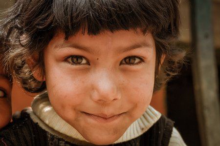 Beni, Nepal - circa May 2012: Young girl with short brown hair and beautiful brown eyes has dirt on cheeks and looks timidly to photocamera in streets of Beni, Nepal. Documentary editorial.のeditorial素材