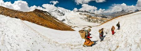 Dolpo, Nepal - circa June 2012: Native man and women carry baskets with heavy load and walk in snow in beautiful snowy mountains in Dolpo, Nepal. Documentary editorial.のeditorial素材