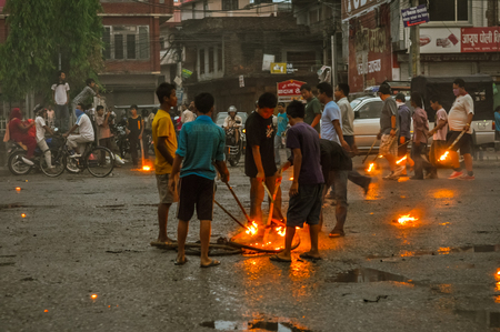 Nepal - circa May 2012: Young boys stand around fireplace on street and burn torches on rainy day during Nepal general strike. Documentary editorial.のeditorial素材