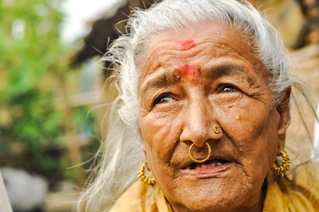 Damak, Nepal - circa May 2012: Old woman with red dots on her forehead and golden piercings in her nose looks up at Nepali refugee camp in Damak, Nepal. Documentary editorial.のeditorial素材
