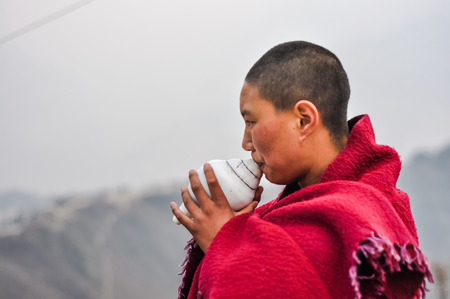 Anigompas, Arunachal Pradesh - circa February 2012: Young monk dressed in red clothes blows seashell in Anigompas, Arunachal Pradesh. Documentary editorial.のeditorial素材