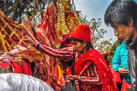 Pathivara Devi, Nepal - circa May 2012: Woman in red clothes touches red and golden cloth in streets of Pathivara Devi, Nepal. Documentary editorial.のeditorial素材