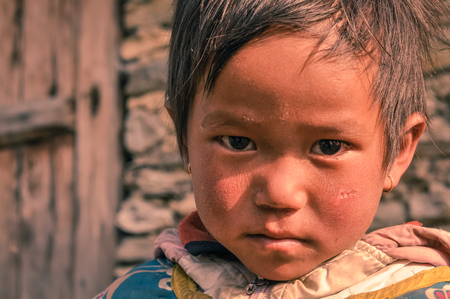 Beni, Nepal - circa May 2012: Small girl with short brown hair and brown eyes wears earrings and looks sadly to photocamera in Beni, Nepal. Documentary editorial.のeditorial素材
