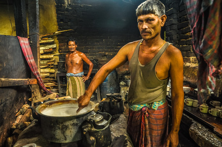 Chittagong, Bangladesh - circa July 2012: Native man stirs food in pot in kitchen in rural village near Chittagong, Bangladesh. In background with halfnaked man. Documentary editorial.のeditorial素材