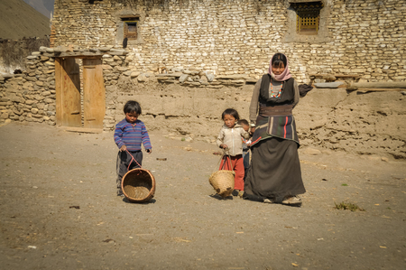 Dolpo, Nepal - circa June 2012: Native woman in brown dress with headcloth with her two young children with small baskets in Dolpo, Nepal. Documentary editorial.のeditorial素材