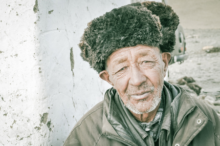 Karakul, Tajikistan - circa September 2011: Older man with wrinkles on his face and with cap made of fur on his head poses in Karakul, Tajikistan. Documentary editorial.のeditorial素材