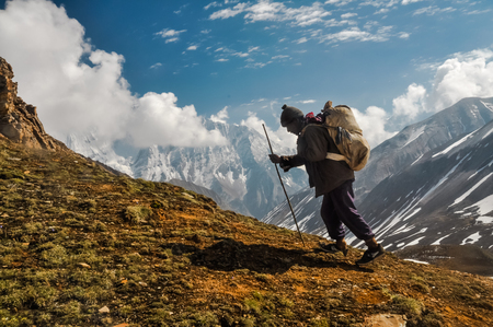 Dolpo, Nepal - circa June 2012: Photo of native man dressed in black clothes with brown bag on his back with wooden stick in hand in Dolpo, Nepal. Documentary editorial.のeditorial素材