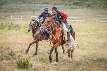 Karakol, Kyrgyzstan - circa July 2011: Two young boys sit on brown horses and play national game at Karakol festival in Kyrgyzstan. Documentary editorial.のeditorial素材