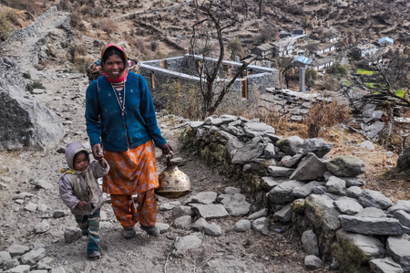 Kuari pass, Uttarakhand - circa December 2011: Smiling native woman in blue sweater and headcloth holds hand of her child and iron pot in left hand in Kuari pass, Uttarkhand. Documentary editorial.のeditorial素材