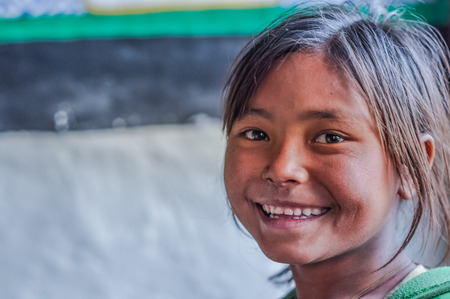Dolpo, Nepal - circa May 2012: Young brown-haired girl smiles nicely to photocamera with brown glittering eyes in Dolpo, Nepal. Documentary editorial.のeditorial素材