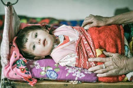 Wakhan valley, Tajikistan - circa October 2011: Small child in colourful clothes lies in bed in Wakhan valley, Tajikistan. Documentary editorial.のeditorial素材