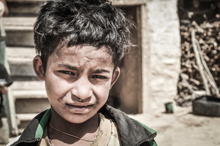 Dolpo, Nepal - circa May 2012: Small black-haired boy with orange necklace frowns and looks sadly to photocamera in Dolpo, Nepal. Documentary editorial.のeditorial素材