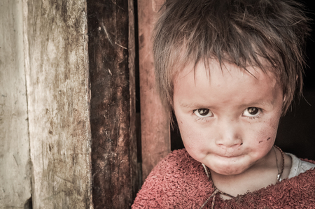 Dolpo, Nepal - circa May 2012: Small girl with brown glittering eyes dressed in red sweater looks curiously up to photocamera in Dolpo, Nepal. Documentary editorial.のeditorial素材