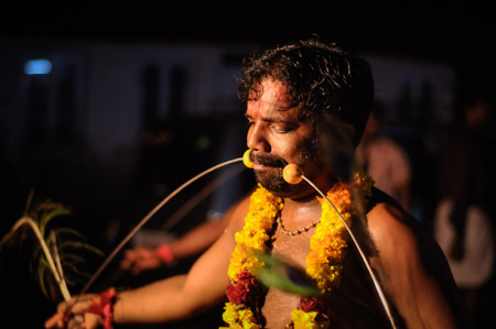 Alleppey, Kerala - circa February 2012: Native man with yellow flowers around his neck holds circle in his mouth and hands during traditional performances in Alleppey, Kerala. Documentary editorial.のeditorial素材