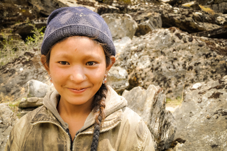 Dolpo, Nepal - circa June 2012: Young brown-haired girl with blue cap and earrings wears brown sweatshirt in beautiful mountains in Dolpo, Nepal. Documentary editorial.のeditorial素材