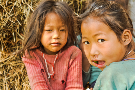 Kanchenjunga Trek, Nepal - circa April 2012: Two young girls sit on ground in Kanchenjunga Trek, Nepal. One of them eats fruit. Documentary editorial.のeditorial素材