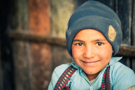 Beni, Nepal - circa May 2012: Photo of young native boy with big brown eyes wearing grey cap and blue shirt smiles nicely to photocamera in Beni, Nepal. Documentary editorial.のeditorial素材