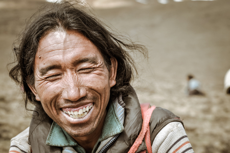Dolpo, Nepal - circa June 2012: Native black-haired man dressed in jacket sits on ground and laughs joyfully with closed eyes in Dolpo, Nepal. Documentary editorial.のeditorial素材