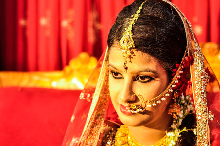 Dhaka, Bangladesh - circa July 2012: Photo of young black-haired bride with piercing and with gold glittering veil on head posing during her wedding in Dhaka, Bangladesh. Documentary editorial.のeditorial素材