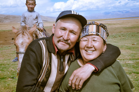 Son Kol, Kyrgyzstan - circa September 2011: Smiling native man poses with his mother in Son Kol, Kyrgyzstan. In the backgroud with young boy on horse. Documentary editorial.のeditorial素材