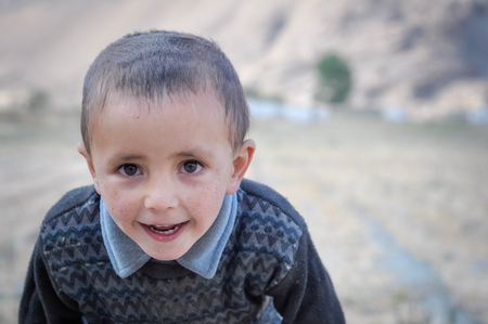 Karakul, Tajikistan - circa September 2011: Small boy with dust on his face looks curiously to photocamera in Karakul, Tajikistan. Documentary editorial.のeditorial素材