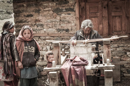 Dolpo, Nepal - circa June 2012: Young men sit on stones with bag and baskets on their backs in background with beautiful mountains covered in snow in Dolpo, Nepal. Documentary editorial.のeditorial素材