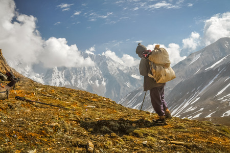 Dolpo, Nepal - circa June 2012: Native man dressed in black clothes with black cap on head and brown bag walks up hill in Dolpo, Nepal. Documentary editorial.のeditorial素材