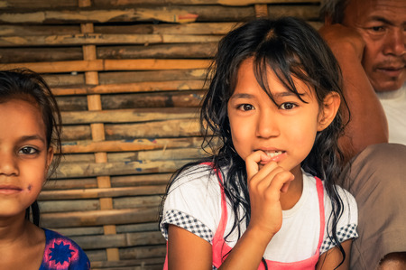 Damak, Nepal - circa May 2012: Young girl with long brown hair and with finger in her mouth looks curiously to photocamera at Nepali refugee camp in Damak, Nepal. Documentary editorial.のeditorial素材