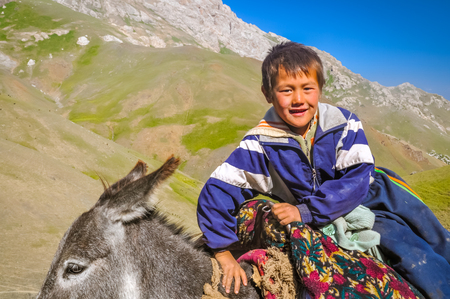 Arslanbob, Kyrgyzstan - circa July 2011: Young native boy sits on donkey in Arslanbob, Kyrgyzstan. Documentary editorial.のeditorial素材
