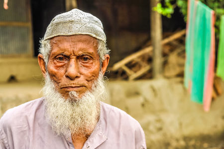 Paigacha, Bangladesh - circa July 2012: Old man with short white hair and long white beard wears white cap and shirt in Paigacha, Bangladesh. Documentary editorial.のeditorial素材