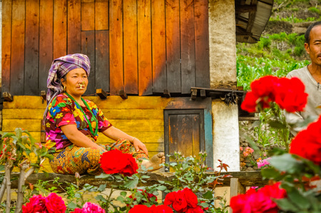 Kanchenjunga Trek, Nepal - circa May 2012: Woman with headcloth and large piercing in her nose sits on bench in her garden near house in Kanchenjunga Trek, Nepal. Documentary editorial.のeditorial素材