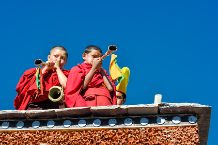 Thiksey, Ladakh - circa November 2011: Two young monks stand at rooftop and play trumpets during Thiksey festival in Ladakh. Documentary editorial.のeditorial素材