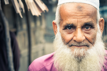 Paigacha, Bangladesh - circa July 2012: Old man with long white beard dressed in pink shirt and white cap with interesting brown and blue eyes in Paigacha, Bangladesh. Documentary editorial.のeditorial素材