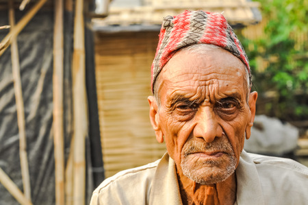 Damak, Nepal - circa May 2012: Old man with wrinkled face with cap on his head frowns and looks sadly to photocamera at Nepali refugee camp in Damak, Nepal. Documentary editorial.のeditorial素材