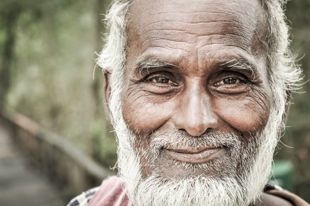 Sunderban, Bangladesh - circa July 2012: Old native man with white beard and hair wears colourful scarf and brown shirt and holds wooden stick in hand in Sunderban, Bangladesh. Documentary editorial.のeditorial素材