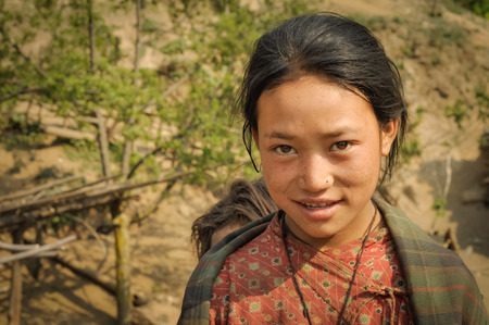 Dolpo, Nepal - circa May 2012: Young black-haired girl with brown eyes dressed in red shirt smiles gently in Dolpo, Nepal. Documentary editorial.のeditorial素材