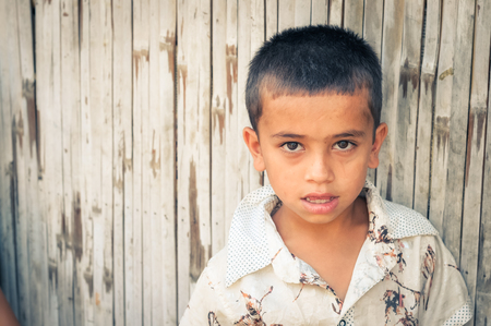 Damak, Nepal - circa April 2012: Young boy in white shirt stands in front of wooden wall at Nepali refugees camp in Damak, Nepal. Documentary editorial.のeditorial素材