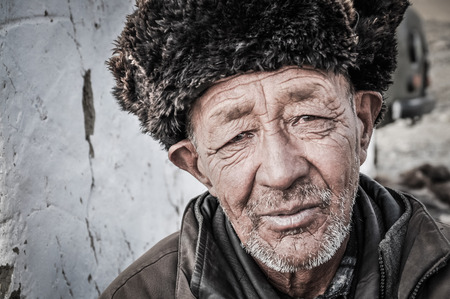Karakul, Tajikistan - circa September 2011: Older man with wrinkled face and with cap made of fur on his head in Karakul, Tajikistan. Documentary editorial.のeditorial素材