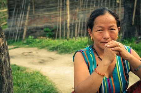 Damak, Nepal - circa May 2012: Brown-haired woman in colourful t-shirt sits with joined hands at Nepali refugee camp in Damak, Nepal. Documentary editorial.のeditorial素材