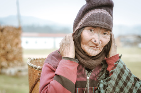 Ziro, Arunachal Pradesh - circa March 2012: Photo of Apatani woman with typical tattoo and large nose plugs who carries wicker basket in Ziro, Arunachal Pradesh. Documentary editorial.のeditorial素材