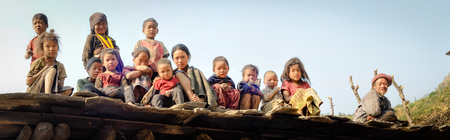 Dolpo, Nepal - circa May 2012: Native children and old man sit in row on roof of house and look down to photocamera in Dolpo, Nepal. Documentary editorial.のeditorial素材