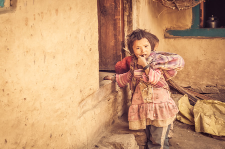 Dolpo, Nepal - circa May 2012: Small brown-haired girl dressed in pink clothes stands on doorstep and puts her finger in her mouth in Dolpo, Nepal. Documentary editorial.のeditorial素材