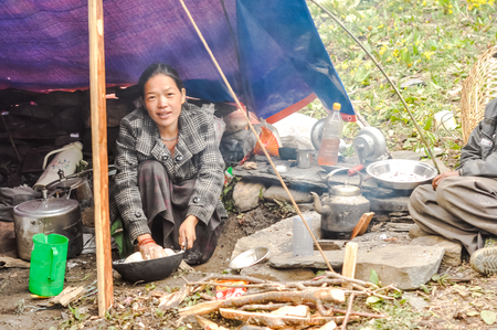 Dolpo, Nepal - circa May 2012: Young woman in black and white jacket kneels on ground and prepares meal under simple shelter in Dolpo, Nepal. Documentary editorial.のeditorial素材