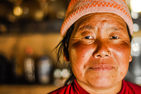Kanchenjunga Trek, Nepal - circa May 2012: Woman with red cheeks and golden piercing in her nose wears cap on her head in Kanchenjunga Trek, Nepal. Documentary editorial.のeditorial素材
