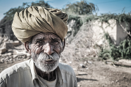 Jaisalmer, Rajasthan - circa December 2011: Native old man with tanned wrinkled face and grey beard wears turban in Thar desert on camel, Jaisalmer, Rajasthan. Documentary editorial.のeditorial素材