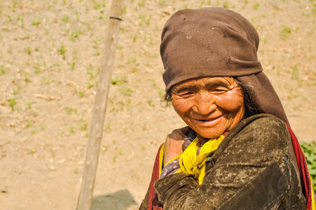 Dolpo, Nepal - circa May 2012: Old native woman with wrinkled face and brown headcloth looks down and smiles nicely in Dolpo, Nepal. Documentary editorial.のeditorial素材