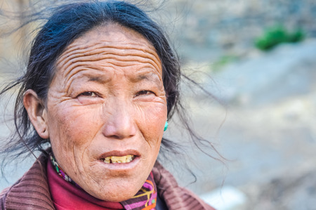Dolpo, Nepal - circa June 2012: Native black-haired woman with wrinkles on forehead dressed in red shirt wears one blue earring in Dolpo, Nepal. Documentary editorial.のeditorial素材