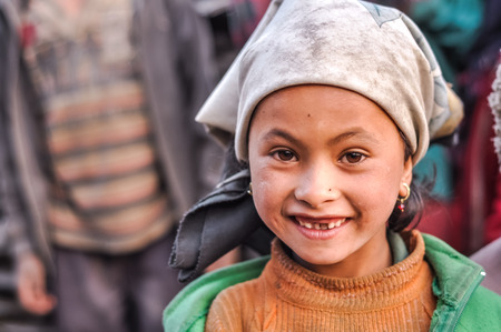 Dolpo, Nepal - circa May 2012: Young brown-eyed girl with earrings wears white headcloth and yellow sweatshirt in Dolpo, Nepal. Documentary editorial.のeditorial素材